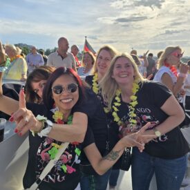 Gäste mit Getränken auf dem sonnigen Freideck eines Partyschiffs